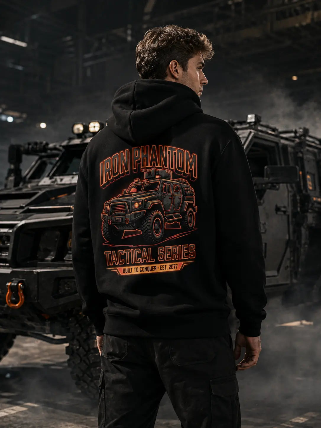 IRON PHANTOM Tactical Series Cyberpunk Armored Vehicle Hoodie - back view on male model in dark moody industrial warehouse with military armored vehicles, orange cyberpunk tactical vehicle graphic print visible