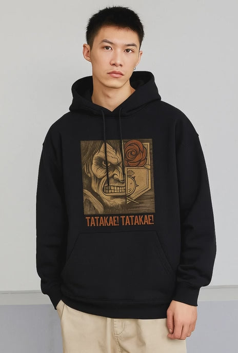 A smiling Asian male model wearing a black hoodie featuring a split graphic of a fierce, roaring titan face and the Wings of Freedom (Survey Corps) logo. The words "TATAKAE! TATAKAE!" are printed below the graphic.